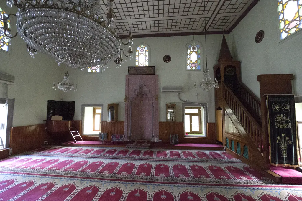 Defterdar Camii'nin içi; geniş kırmızı halı, kristal avize, mihrap, minber ve ahşap kaplı alt duvarlar.