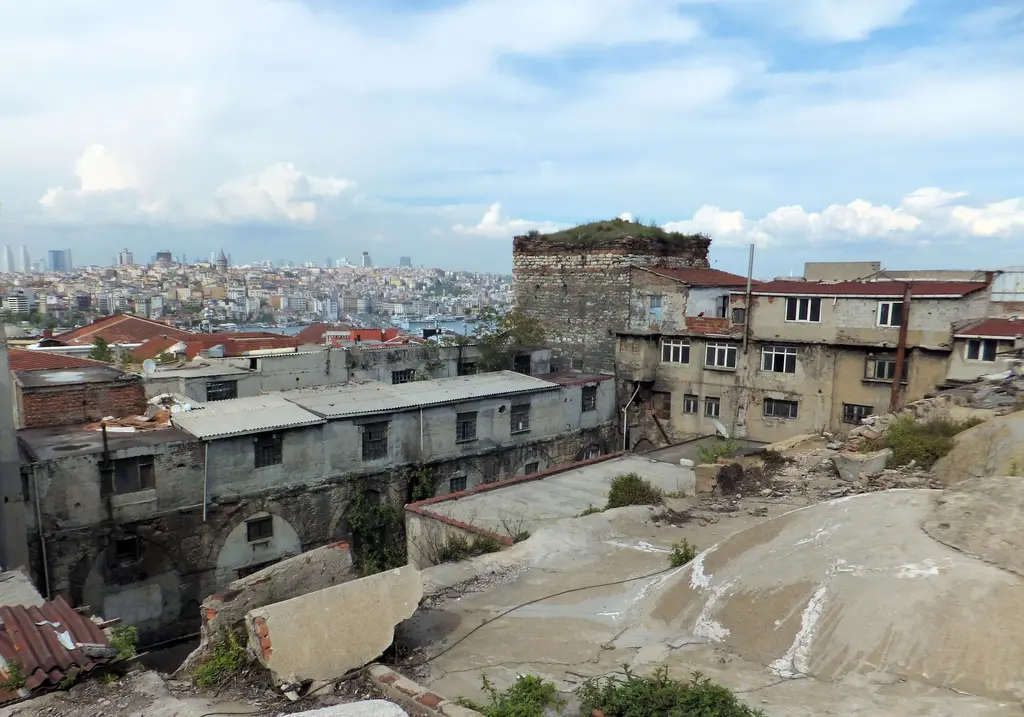 Büyük Valide Han'ın çatısından kuzeydeki küçük avluya bakış; önde sıvalı kubbeler, ortada otların bürüdüğü kare kesitli taş kule, arkada Haliç ve şehir silueti.