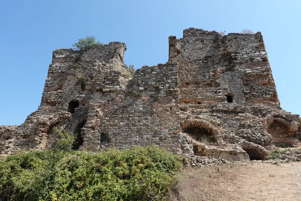 Yoros Kalesi'nin batı duvarı; yıkık taş ve tuğla kule kalıntıları, kemerli açıklıklar ve önde çalılar.
