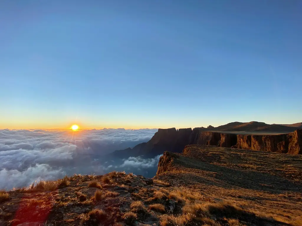 Güney Afrika'da Drakensberg Dağları; bulut denizinin üzerinde doğan güneş ve altın rengi ışıkta uzanan yüksek yayla uçurumları.