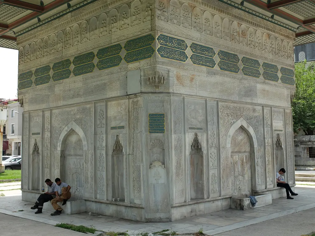 Tophane Çeşmesi'nin bir cephesi; ortada niş ve önündeki mermer yalak, yanlarda küçük nişler, kaide boyunca oturan insanlar.