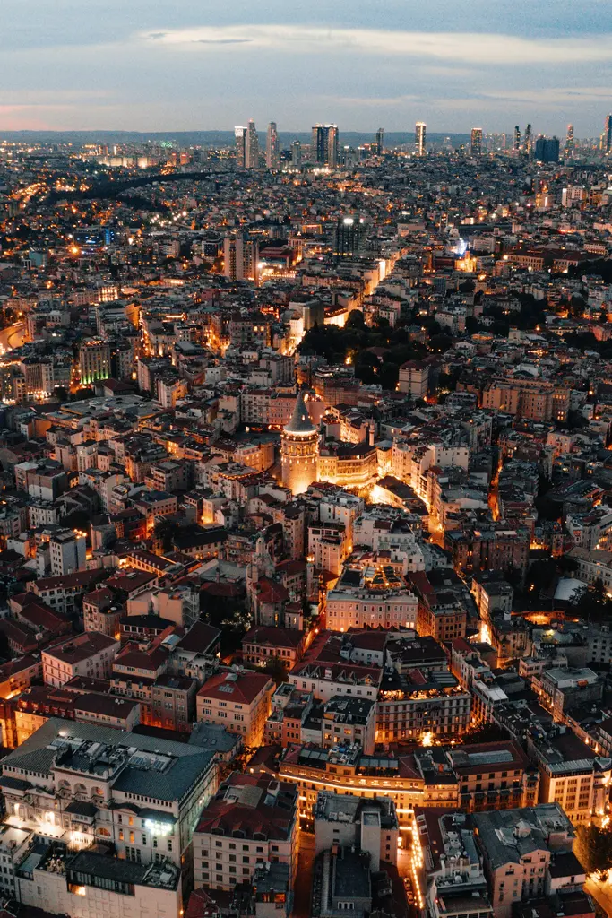 Beyoğlu'nda gece havadan kent dokusu; ışıklı sokaklarla bölünen yoğun yapı adaları, ortada aydınlatılmış Galata Kulesi ve ufukta gökdelenler.