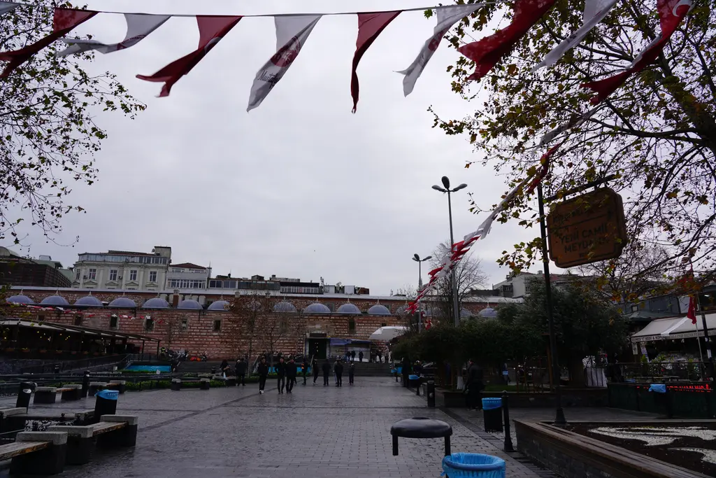 Mısır Çarşısı'nın dış cephesi; kemerli taş yapı, önünde meydan, flamalar, ağaçlar ve kapalı gökyüzü.