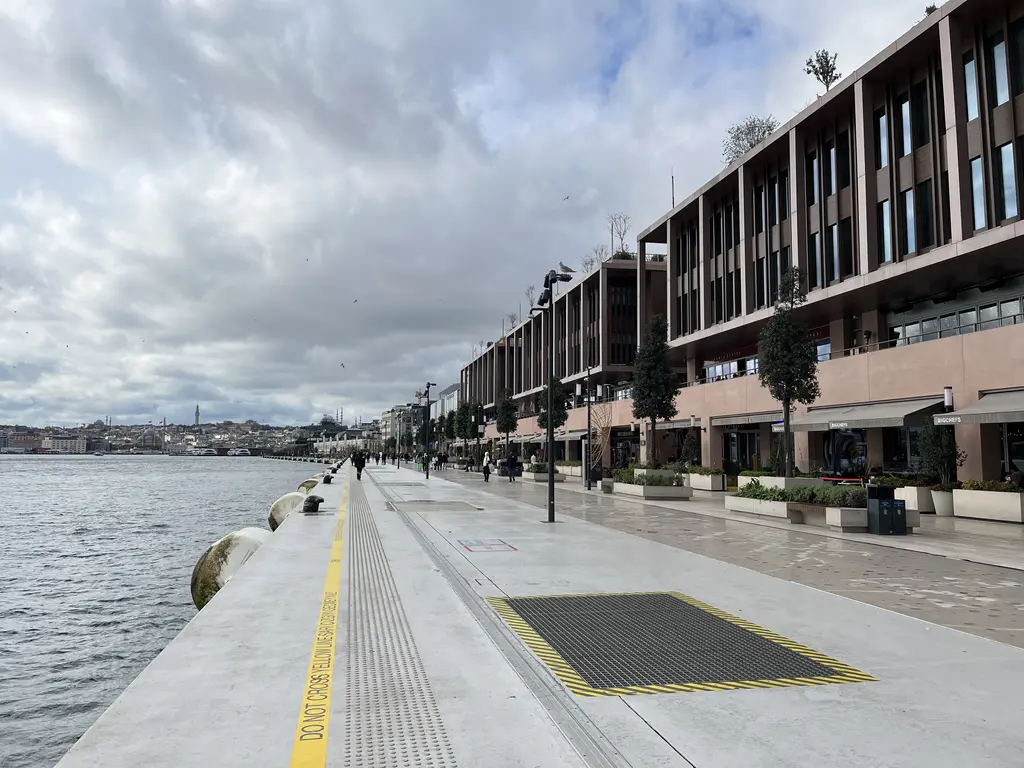 Galataport'ta kıyı yolu Karaköy yönünde; sağda binalar ve ağaçlar, solda Boğaz ve uzakta tarihi yarımada.