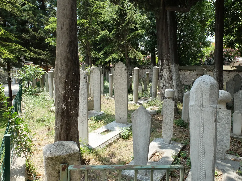 Hazire; sık dizilmiş mermer mezar taşları, kavuklu ve sarıklı başlıklar, çevrede servi ağaçları ve arkada avlu duvarı.