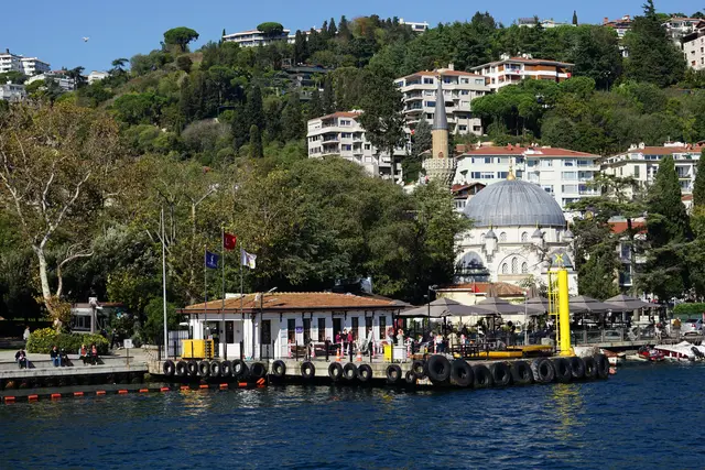 Bebek'te Boğaz'dan koy; kıyıda iskele binası, arkasında kubbeli ve tek minareli Bebek Camii, yamaçta ağaçlar ve evler.