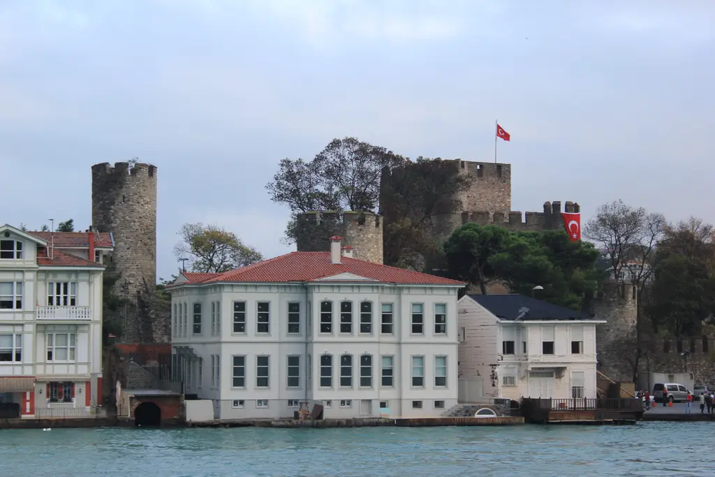 Denizden Anadolu Hisarı; önde büyük beyaz yalı, arkada bayraklı iç kale ve yuvarlak kule.