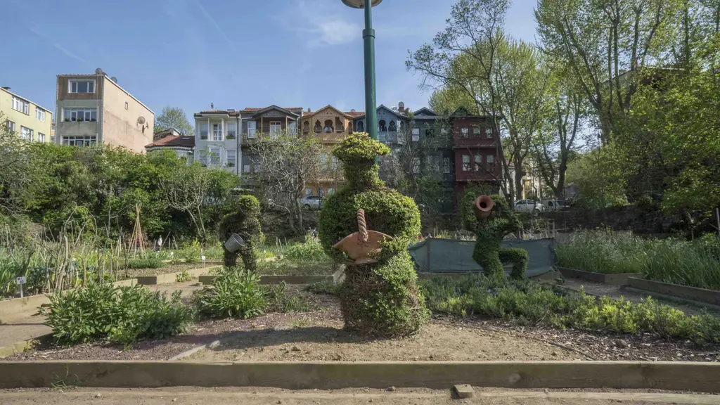 Kuzguncuk Bostanı'nda yeşil bitkiden budanmış figürler; tarhlar, ağaçlar, arkada evler ve sokak lambası.