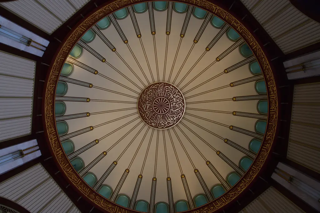 Taksim Camii'nin giriş bölümünde bir kubbe; ışınsal dilimler, kenarda yeşil daire pencereler ve ortada yuvarlak hat yazısı.