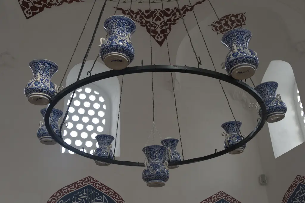 İç mekânda tavandan sarkan halka biçimli avize; üzerinde mavi beyaz çini kandiller, arkada kubbe eteğinde kalem işi bezeme.