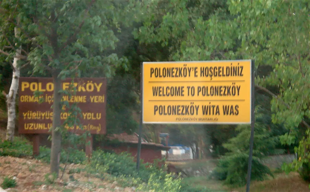 Polonezköy'ün girişinde ağaçlar arasında sarı tabela; üstünde Türkçe, İngilizce ve Lehçe "Polonezköy'e hoş geldiniz" yazısı, yanında orman dinlenme yeri levhası.
