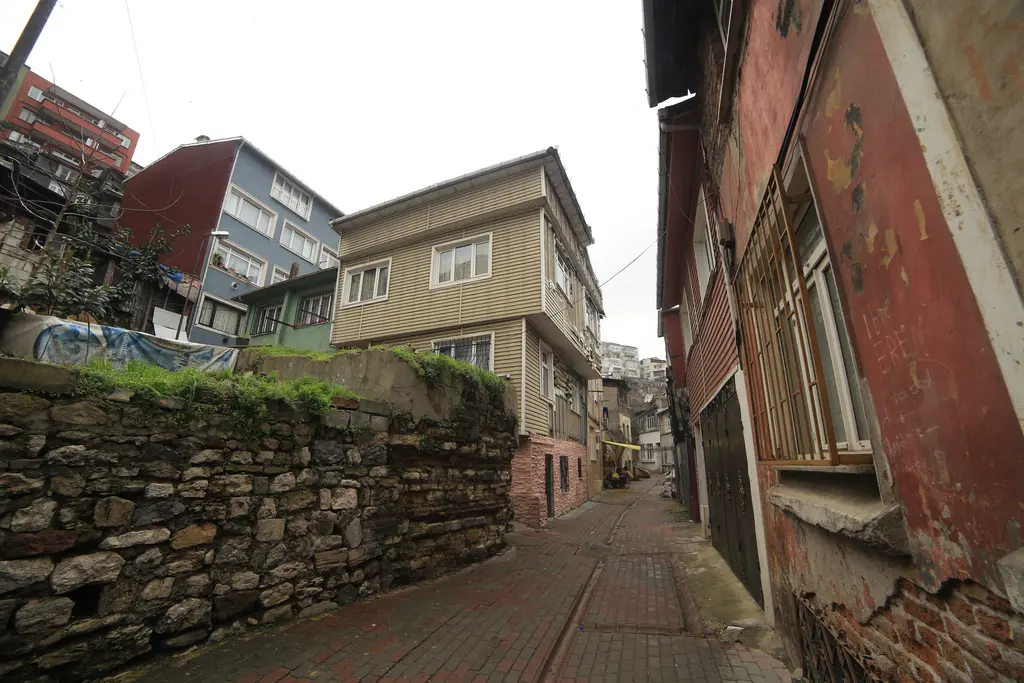 Fener'de Çukur Mescit Sokağı; solda yosunlu taş istinat duvarı, renkli apartmanlar ve dar yokuş.