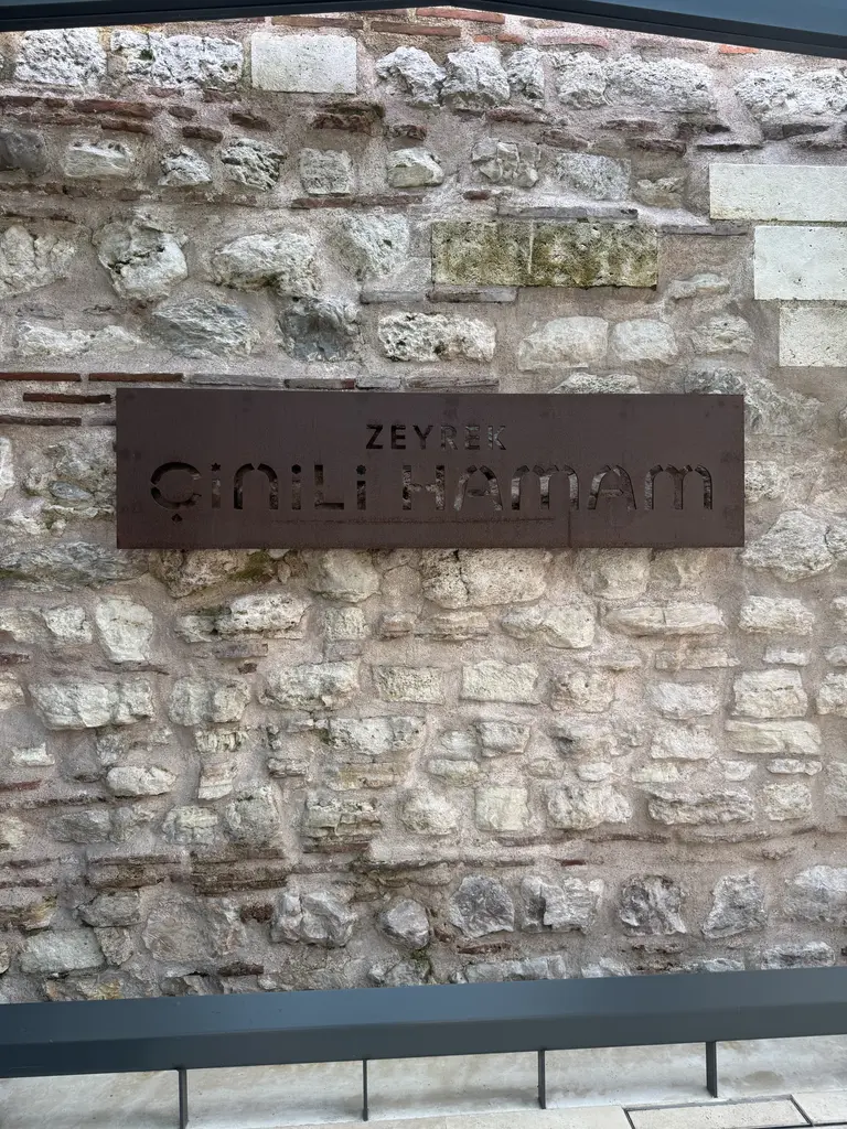 Çinili Hamam'ın tabelası; moloz taş duvara asılı kesme metal harflerle Zeyrek Çinili Hamam yazısı, altında cam korkuluk.