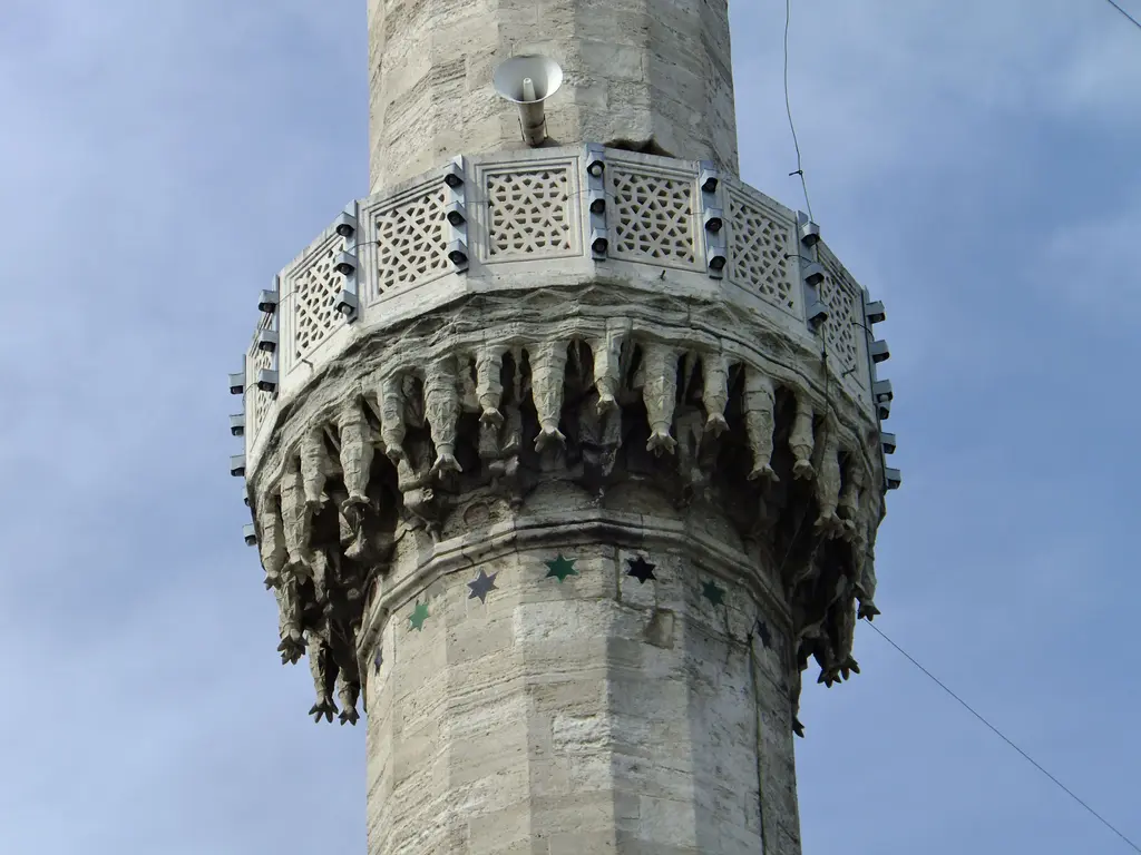 Eyüp Sultan Camii'nin minaresi; yakından mukarnaslı şerefe altı, oymalı taş korkuluk ve mavi gökyüzü.