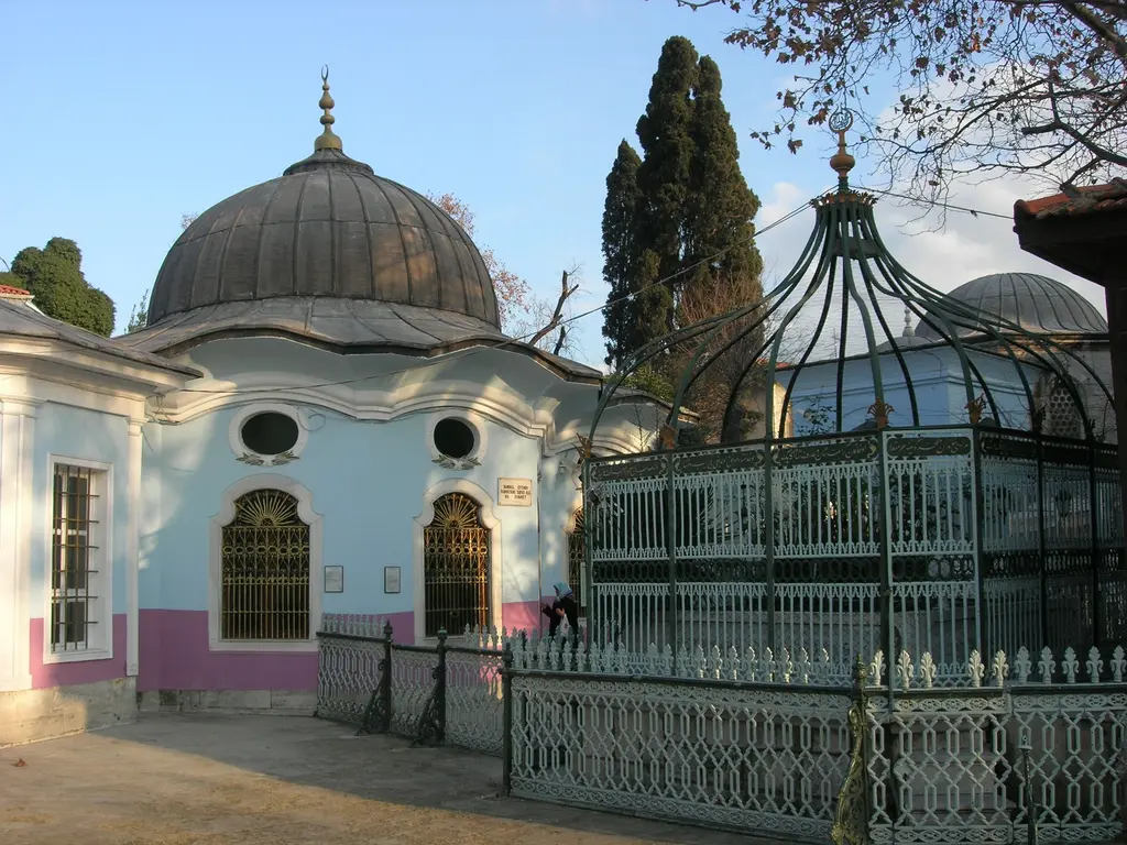 Koca Mustafa Paşa Külliyesi'nde iki türbe; solda pembe etekli beyaz mavi türbe ile kurşun kubbesi, sağda yeşile boyalı dövme demirden kubbe biçimli kafes ve içindeki açık kabirler.
