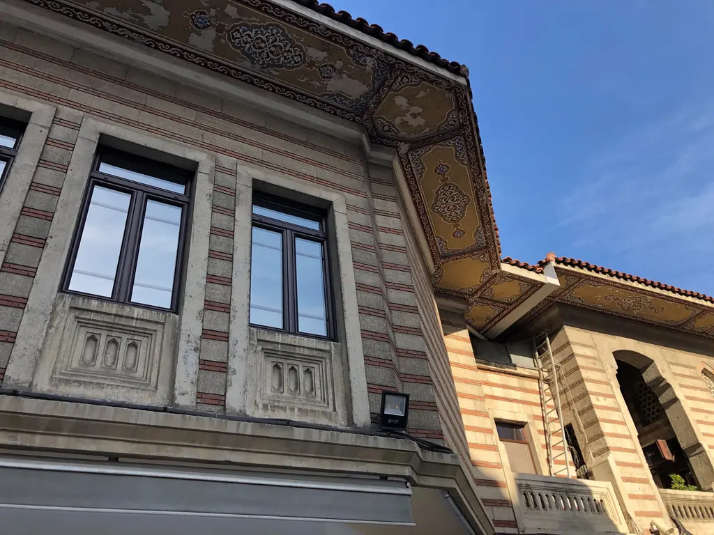 Şişli Camii kütüphane binasının köşesi; kalem işi süslü geniş saçak, çizgili taş duvar, pencereler ve mavi gökyüzü.