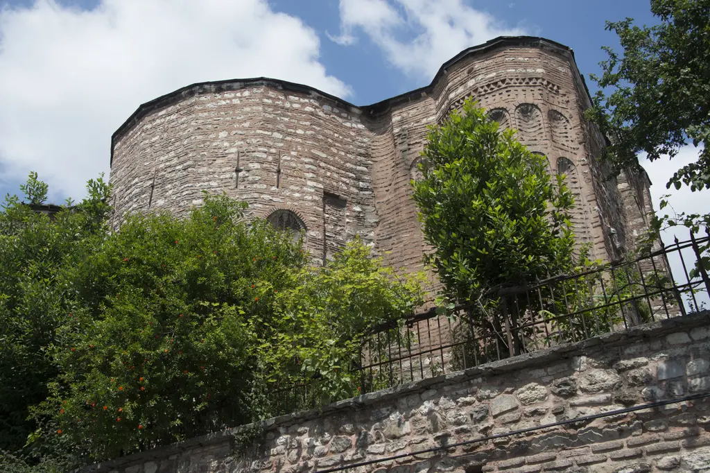 Gül Camii'ne güneydoğudan bakış; yan yana yükselen apsisler, yan apsiste testere dişi tuğla silme, önde demir korkuluk ve yeşil dallar.