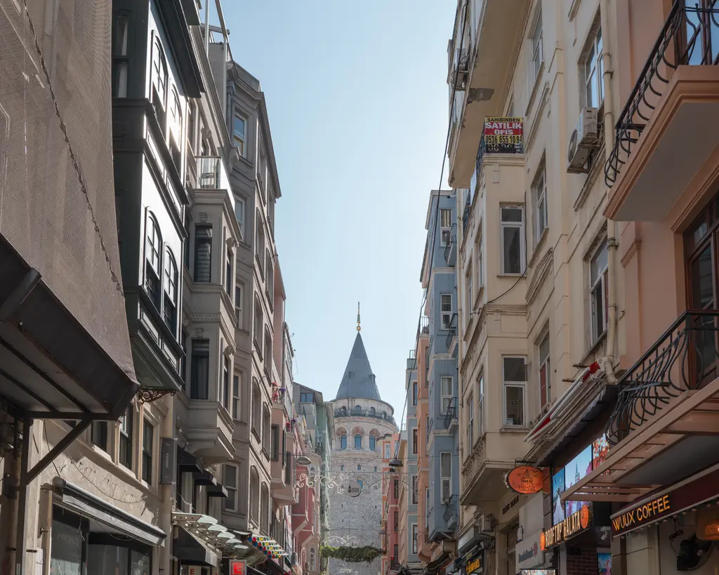 Büyükhendek Caddesi'nden Galata Kulesi; iki yanda eski apartmanlar, kaldırımda yürüyen insanlar ve sokağın ucunda kule.