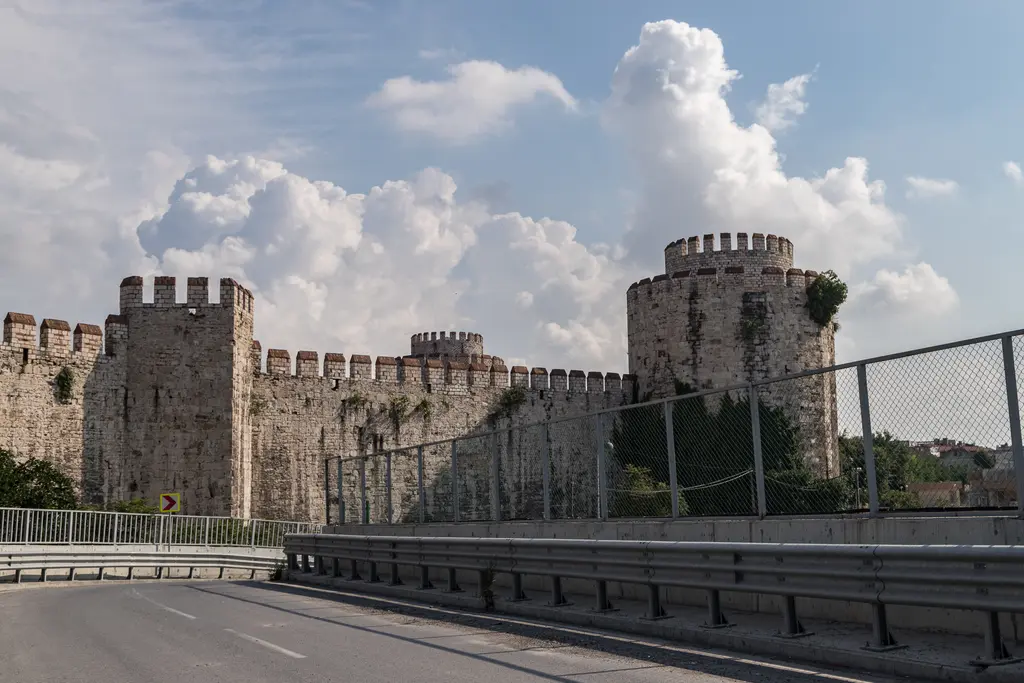 Onarılmış uzun bir sur bölümü; mazgallı siperler, art arda dizilen kuleler ve duvarın hemen dibinden geçen asfalt yol ile bariyer.