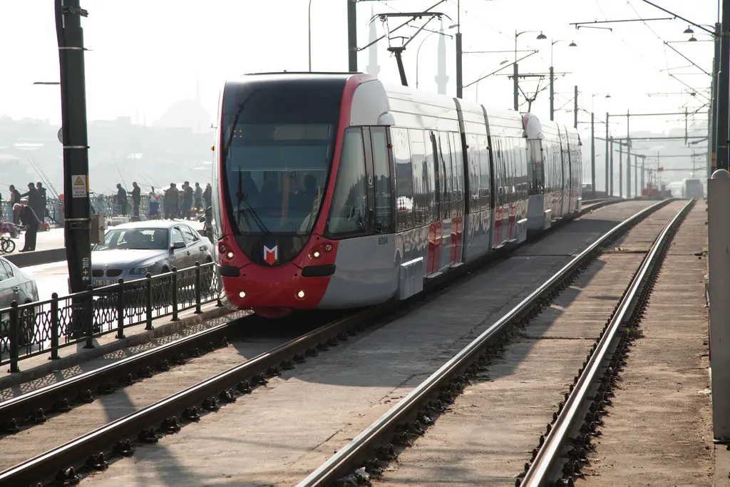 Galata Köprüsü'nde T1 tramvayı; kırmızı beyaz modern tramvay, raylar, elektrik direkleri ve yanda korkuluk.