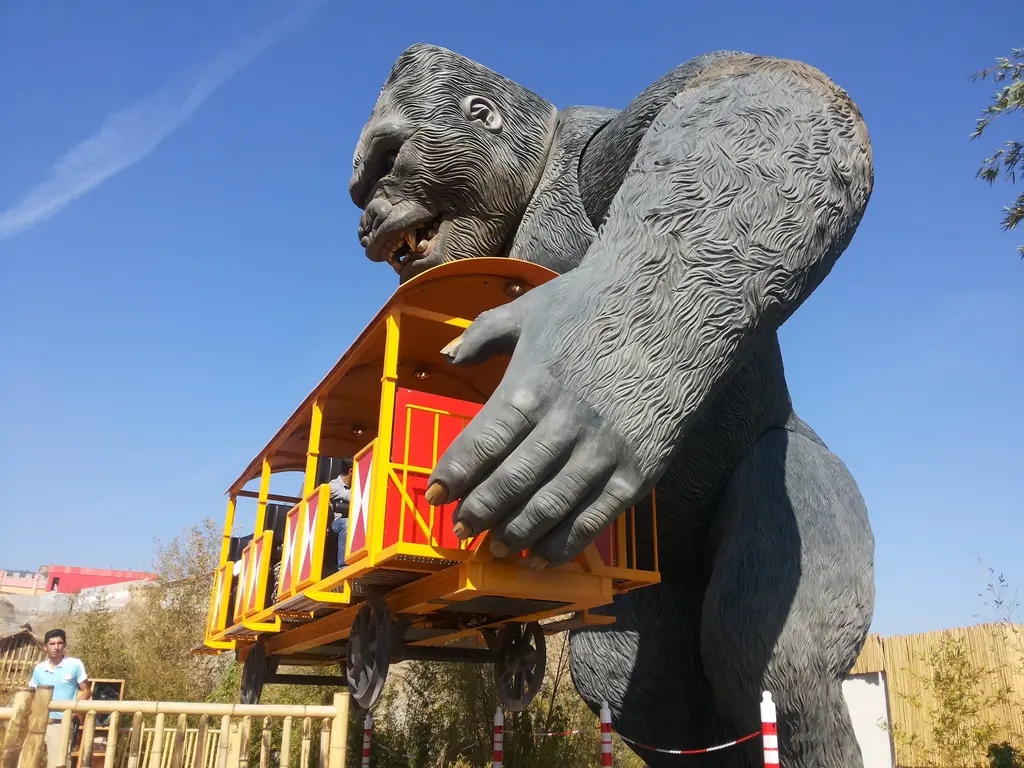 Vialand'de gri dev goril heykeli; elinde kırmızı sarı bir tren vagonunu tutuyor, arkada kırmızı roller coaster rayları ve açık gökyüzü.