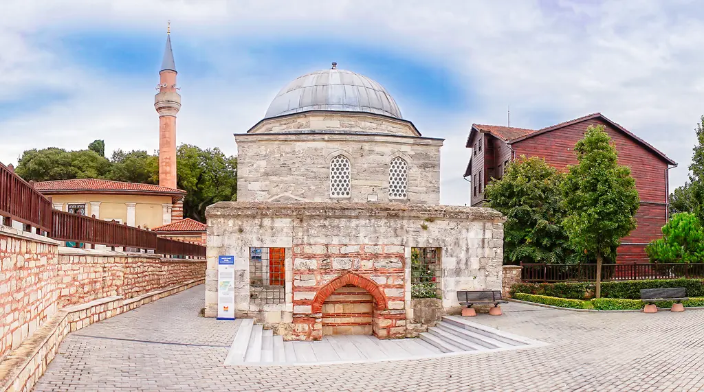 Dârülkurrâ binası; kesme taş duvarlar, kurşun kubbe, kemerli pencereler ve önünde tuğla örgülü avlu duvarı ile ağaçlar.