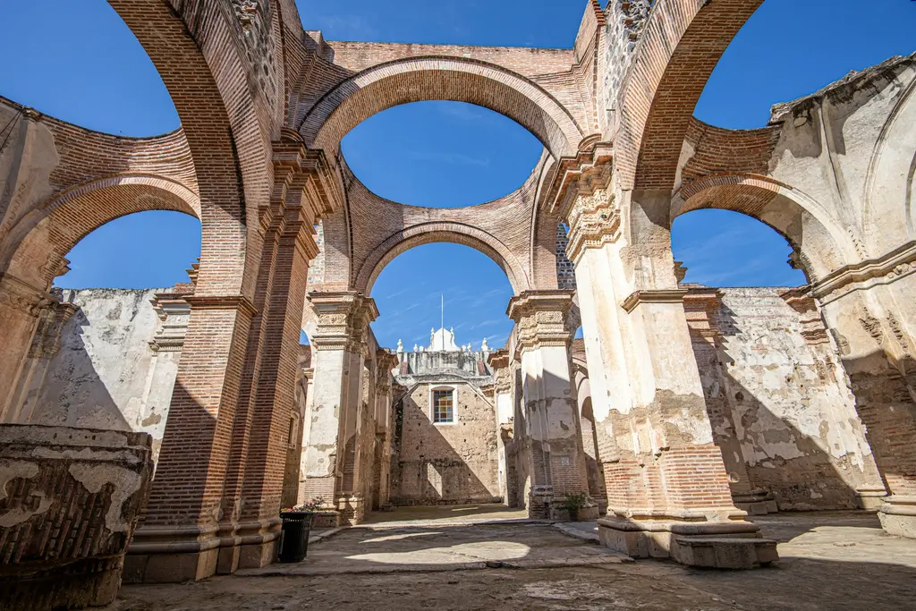 Antigua Guatemala'da depremde yıkılan sömürge dönemi katedralinin kalıntıları; tuğla kemerler ve dökülmüş sıvalı sütunlar arasından görünen berrak mavi gökyüzü.