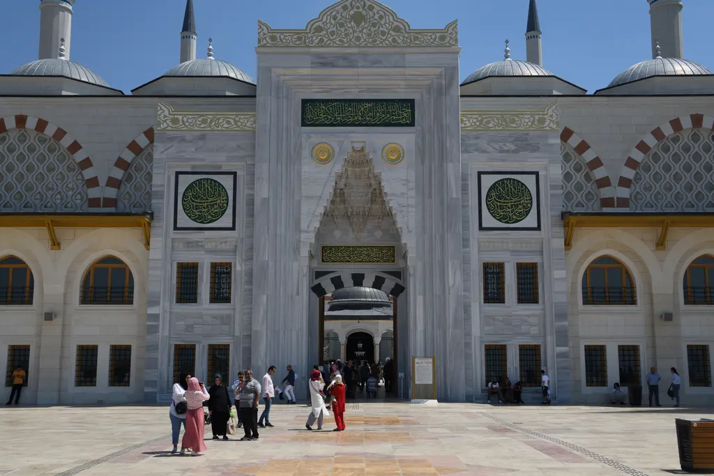 Büyük Çamlıca Camii'nin taçkapısı; mermer cephe, mukarnaslı giriş nişi, yeşil yazı levhaları ve ziyaretçiler.