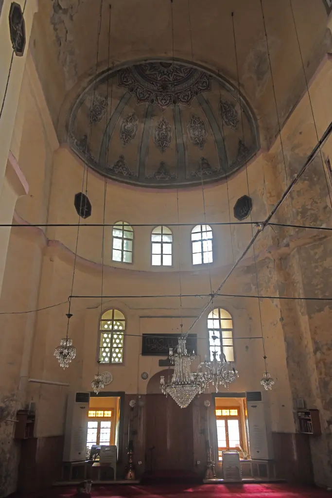 Gül Camii'nde harimden ana apsise bakış; kalem işli yarım kubbe, üç kemerli pencere, altta ahşap lambrili mihrap duvarı ve halıda bir kedi.
