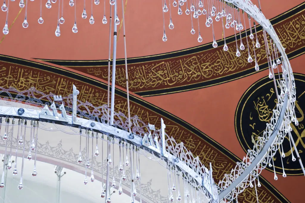 Şakirin Camii'nde avize; aşağıdan bakışla iç içe halkalardan sarkan cam damlalar, kubbe yazıları ve kırmızı zemin.