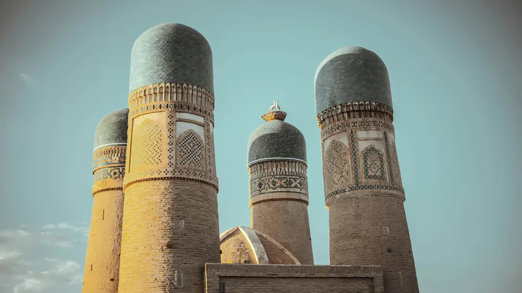 Buhara'da Çar Minar yapısının dört küçük mavi kubbeli kulesi ve aralarındaki kemerli kapı; mütevazı avlu.
