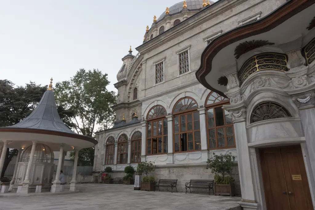 Nusretiye Camii'nin şadırvan avlusu; solda sivri külahlı sütunlu şadırvan, ortada kemerli pencereli yan cephe, sağda dalgalı saçaklı sebil.
