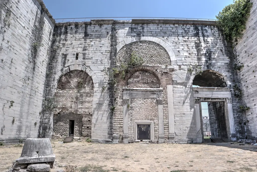 Yedikule Hisarı'nda Altın Kapı'nın avluya bakan yüzü; üstte büyük kemerli niş, altında mermer söveli kapı açıklığı, sağda demir parmaklıklı geçit ve önde toprak zemin.