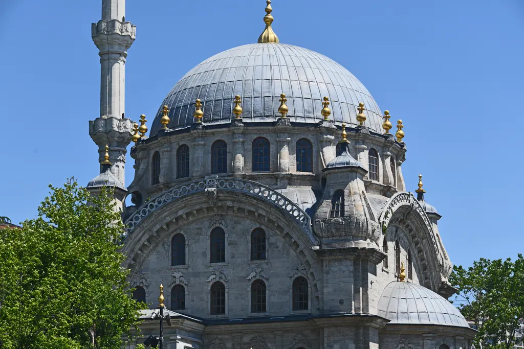 Nusretiye Camii'nin kubbesi; yakın çekimde kurşun kaplı kubbe, tepedeki yaldızlı alem, kasnaktaki kemerli pencereler ve arkada minare.