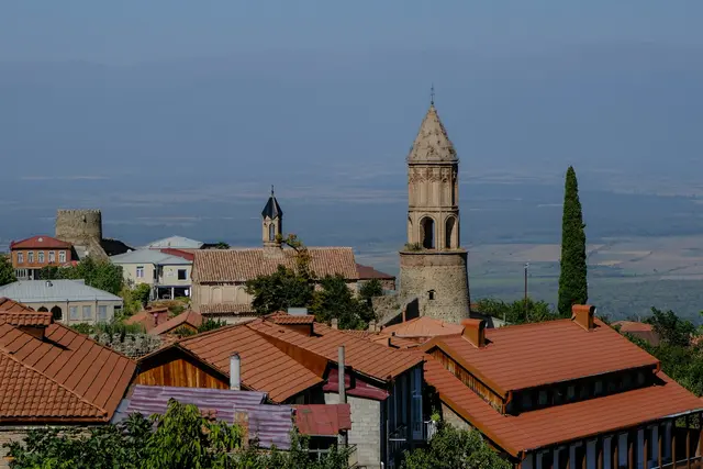 Kakheti'de Sighnaghi kasabası; tepeye kurulu kırmızı çatılı evler, sur duvarı ve arkada Alazani Vadisi ile Kafkas dağları.