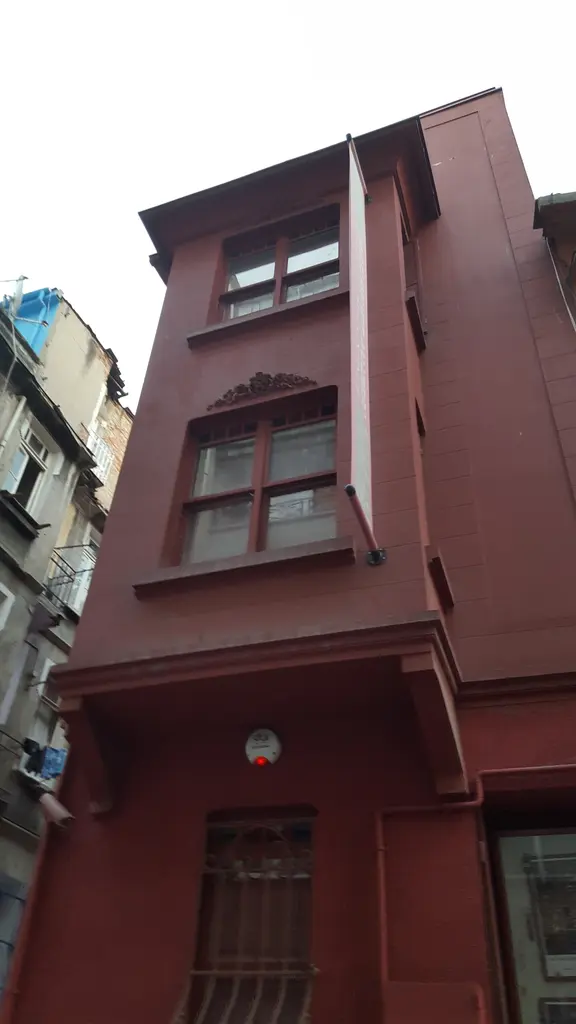 Aşağıdan Masumiyet Müzesi'nin cumbalı cephesi; koyu kırmızı duvarlar, dar pencereler ve mavi gökyüzü.