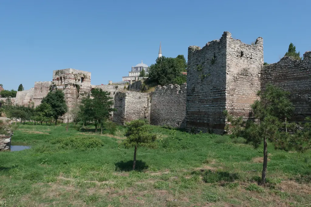 Blakhernai bölümünde sur hattı; tek sıra yüksek duvar, üstündeki kuleler, önündeki çimenlik ve arkada bir caminin kubbesiyle minaresi.