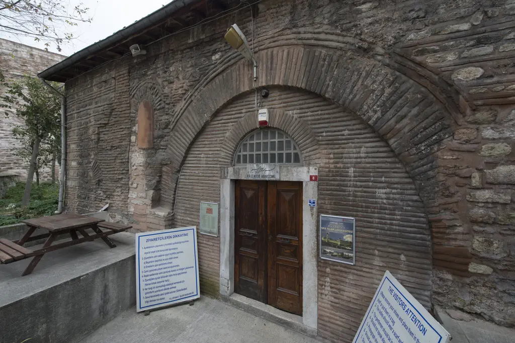 Kalenderhane Camii'nin giriş kapısı; iç içe tuğla kemerli niş, çift kanatlı ahşap kapı, üstünde levha ve önde ziyaretçi bilgi panoları.
