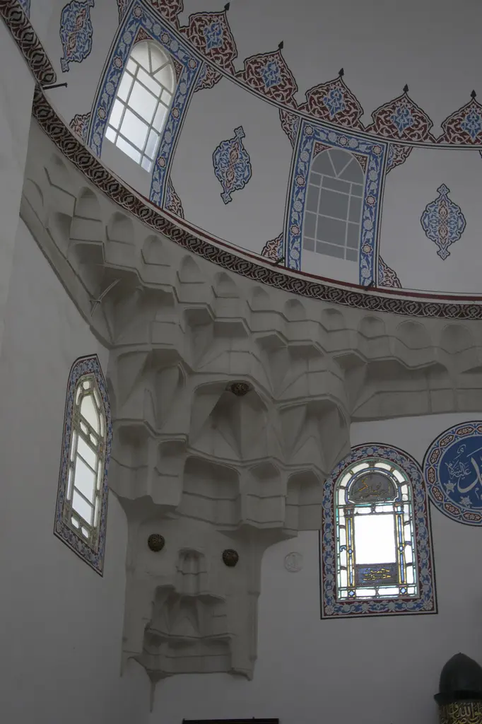 Gazi Atik Ali Paşa Camii'nde köşedeki mukarnaslı pandantif; beyaz sıva, çok katlı mukarnas, çini desenli pencere çerçeveleri.