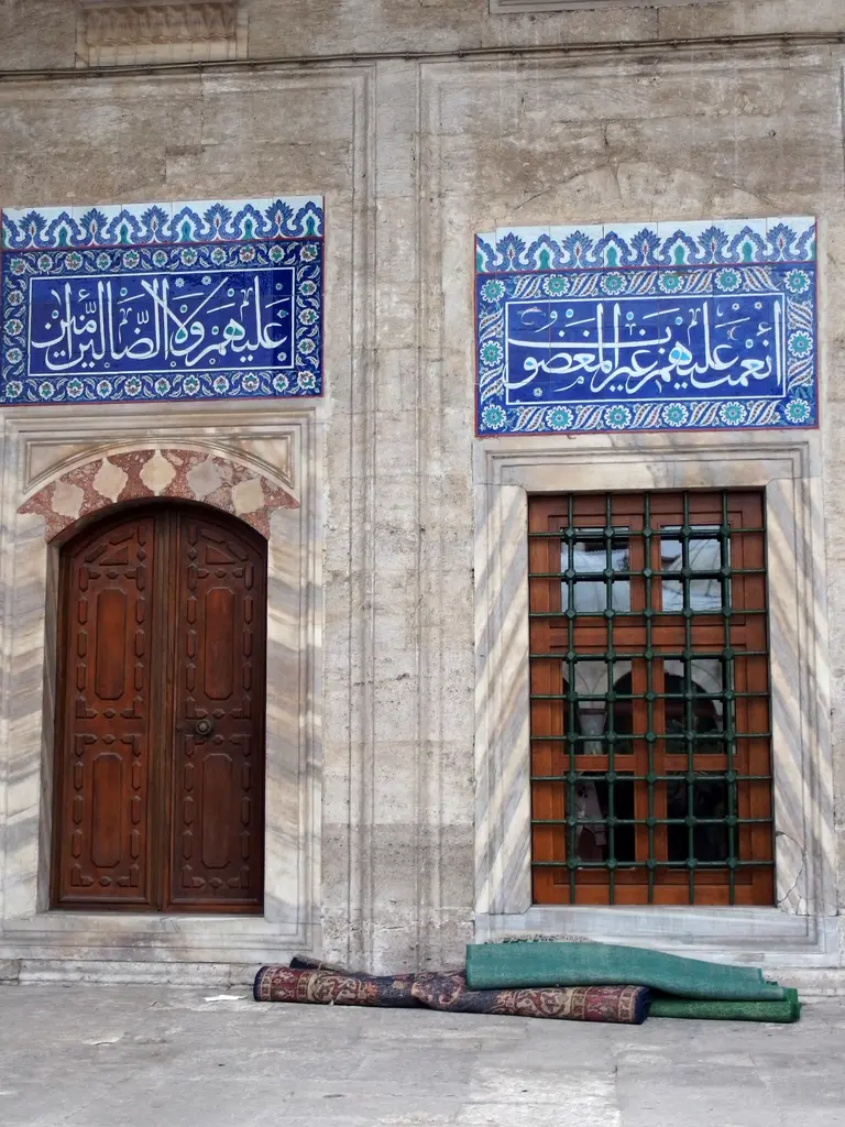 Sokullu Mehmed Paşa Camii'nin cephesinde çini panolar; ahşap kapı, demir parmaklıklı pencere ve üstlerinde iki lacivert hat panosu.