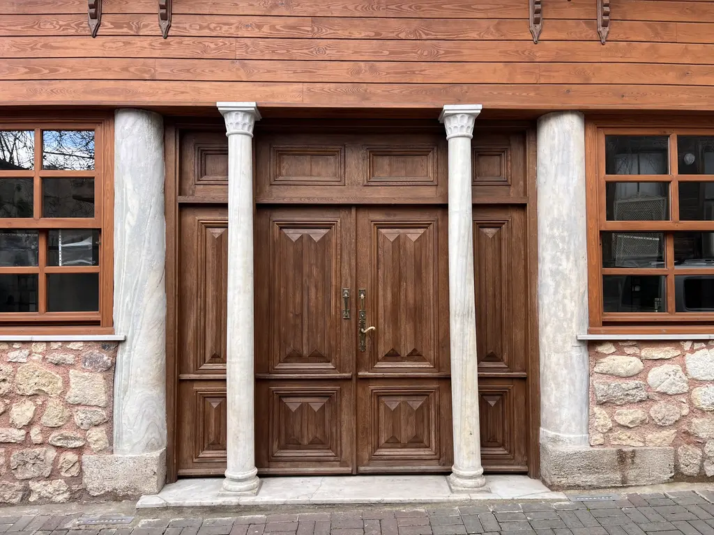 Atik Mustafa Paşa Camii'nin giriş kapısı; ahşap saçak altında iki beyaz mermer sütunun arasında ceviz renkli çift kanatlı ahşap kapı, iki yanda ahşap doğramalı pencereler.