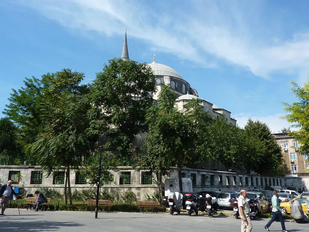 Çemberlitaş'tan Gazi Atik Ali Paşa Camii; önde meydan, banklar ve yayalar, avlu duvarının ardında yeşil ağaçlar, kubbe ve minare.