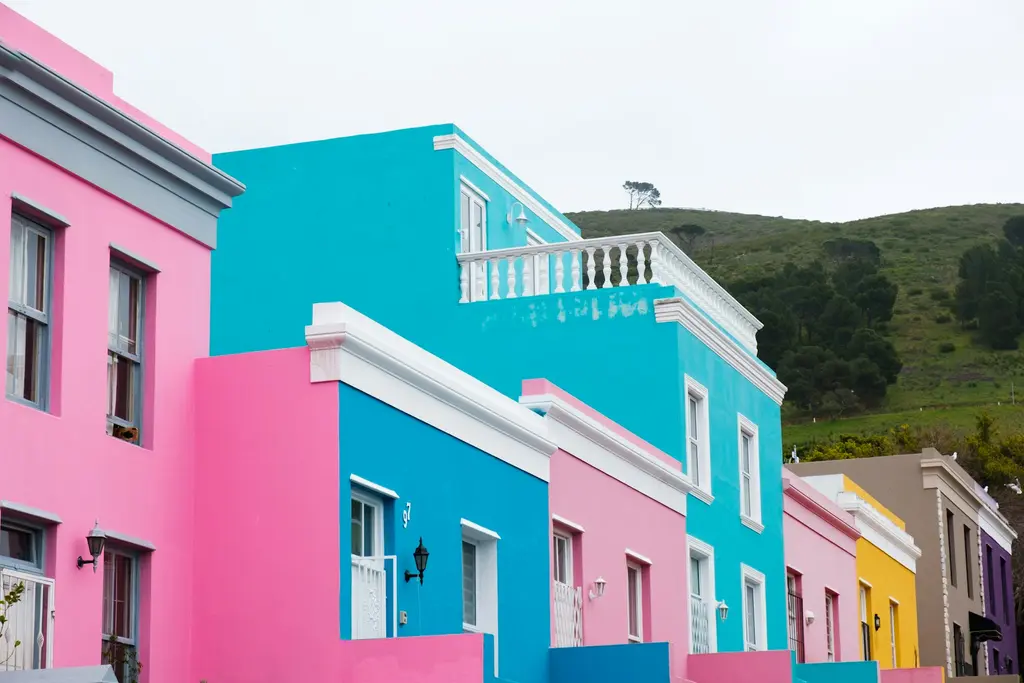 Cape Town'ın Bo-Kaap mahallesinde pembe, turkuaz, mavi ve sarıya boyanmış sıra evler; arkada yeşil bir tepe.