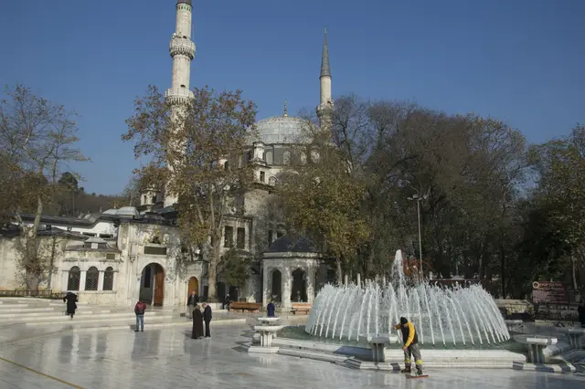 Eyüpsultan'da Eyüp Sultan Camii; iki ince minare, kurşun kubbe, ağaçlar ve önündeki meydanda fıskiyeli havuz.