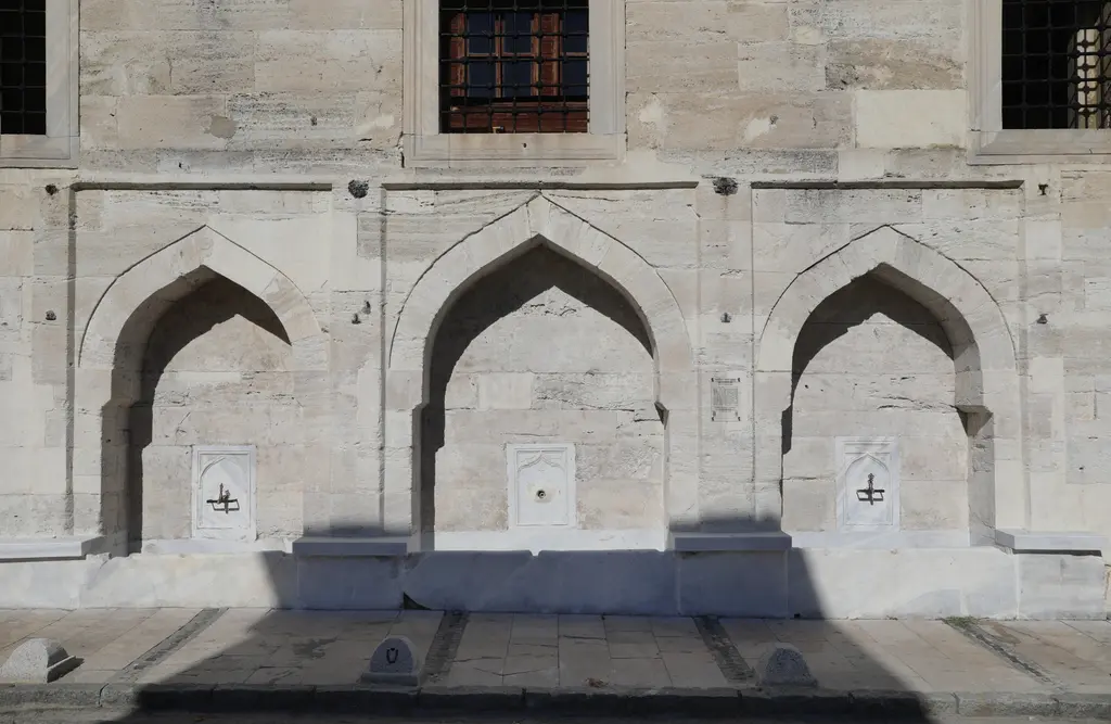 Atik Valide Camii'nin avlu duvarı; kesme taş cephede yan yana üç sivri kemerli çeşme nişi.