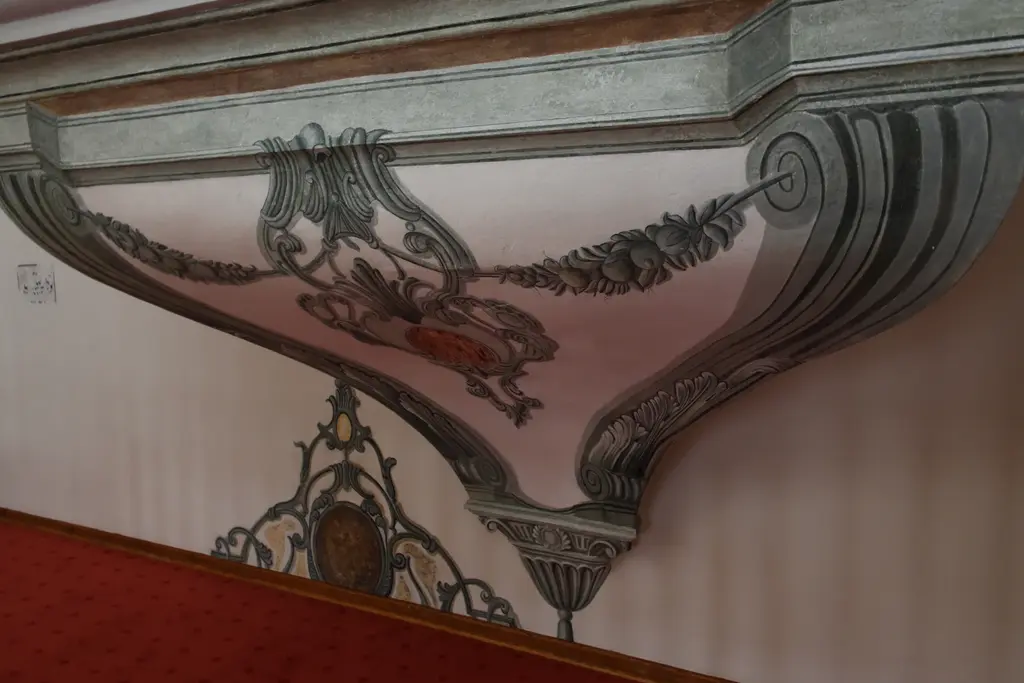 Zeyrek Camii'nde pandantif bezemesi; gri yeşil tonlarda boyanmış kıvrık dallar, meyve çelenkleri, ortada kırmızı madalyon ve altta kırmızı halının kenarı.