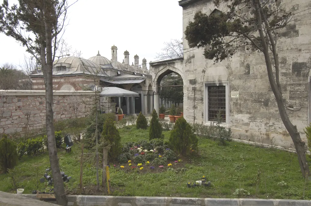Şemsi Paşa Külliyesi'nin avlusu; çiçekli bahçe, ağaçlar, arkada medrese kubbeleri ve bacaları, sağda cami duvarı.