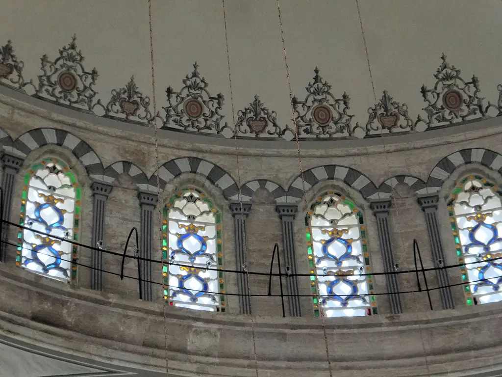 Nuruosmaniye Camii'nde kubbe eteğindeki pencere kuşağı; alaca örülmüş kemerler, mavi ile yeşil renkli camlar ve üstte kıvrımlı barok kartuş frizi.