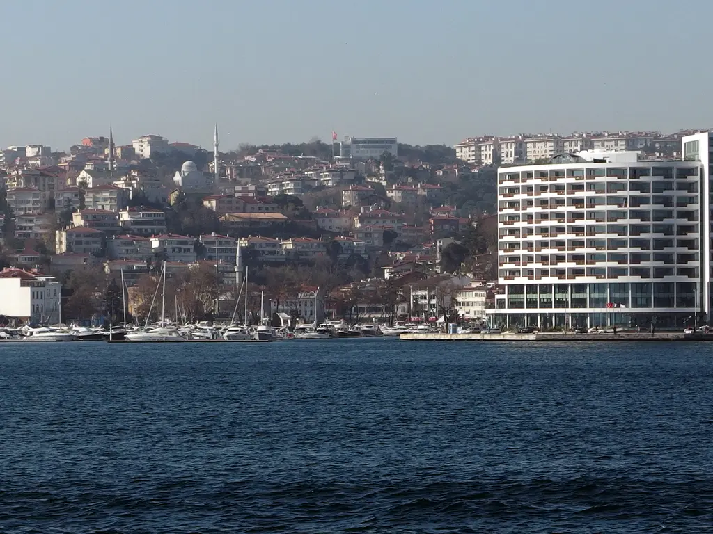 Boğaz'dan Tarabya; kıyıda beyaz çok katlı otel, marinada tekneler, arkada yamaca yayılan evler ve sırtlar.