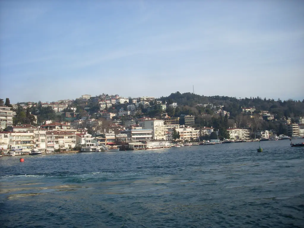 Bebek'te koyun kıyısı; kıyıya dizilen açık renkli binalar, rıhtım, küçük tekneler ve arkada yeşil sırt.
